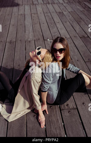 Porträt von zwei modische junge Frauen sitzen auf Holzboden Sonnenbrille tragen Stockfoto