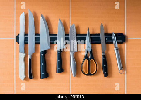 Die Messer hängen an einem Magnethalter. Orangefarbene Küchenwand. Eine Methode zur Aufbewahrung scharfer Gegenstände in der Küche Stockfoto