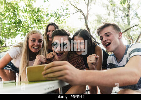 Gruppe der glücklichen Freunde auf der Suche nach Handy im Freien Stockfoto