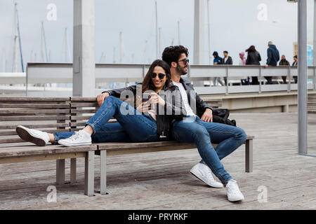 Spanien, Barcelona, glückliches junges Paar mit Handy ruht auf einer Werkbank Stockfoto