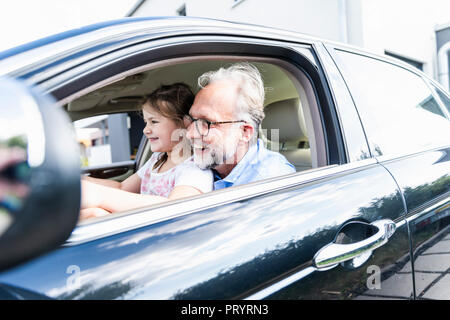 Kleines Mädchen auf den Schoß der Großvater, der vorgibt, das Auto zu lenken Stockfoto