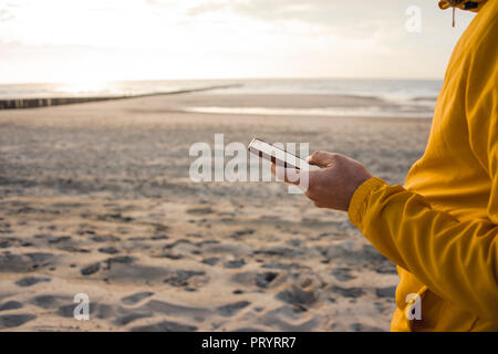 Mann in der gelben Jacke, Sie ihr Smartphone am Strand Stockfoto