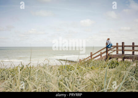 Frau sitzt auf der Zaun am Strand, relaxen am Meer Stockfoto