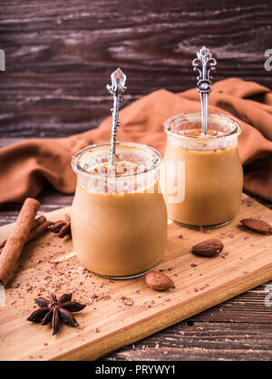 Toffee Karamell Dessert im Glas, bestreut mit geriebener Schokolade. Auf Holzbrett, dekoriert mit Zimtrollen, Mandeln und Sternanis. Rustikal Stockfoto