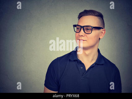 Porträt der jungen legerer Mann in T-Shirt und schwarzer Brille weg schauen auf grauem Hintergrund Stockfoto