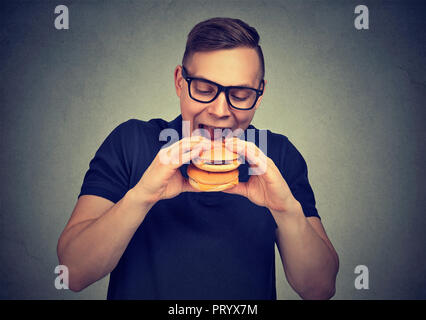 Legerer Mann in Gläsern mit doppelten Cheeseburger aufgeregt beim Verhungern und das Verlangen nach fast food Stockfoto