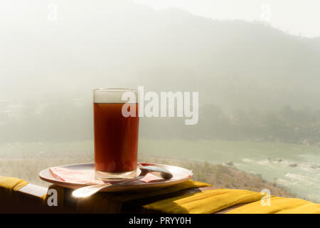 Glas Kaffee mit Berg und Fluss bei Sonnenaufgang. Nebligen eisigen Morgen in den Bergen des Himalaya. Ganges. Rishikesh Indien Stockfoto