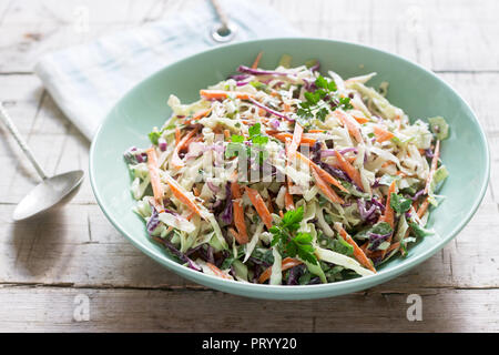 Krautsalat von Kohl, Karotten und verschiedenen Kräutern mit Mayonnaise in einer großen Platte auf einem hölzernen Hintergrund. Stockfoto