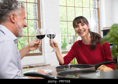Glückliches Paar in der Küche sitzen, Toasten mit rotem Wein, Abendessen genießen. Stockfoto