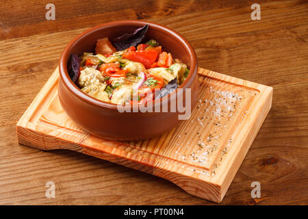 Mit gegrilltem Gemüse Salat - auf Kohle und sautierten in Butter Ghee mit Zwiebeln und Koriander zubereitet. In einem Tontopf auf einem Holzbrett serviert. Stockfoto