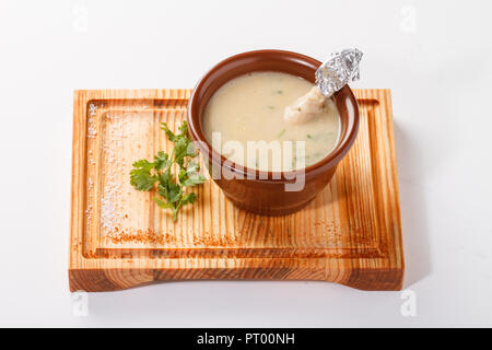 Cremige Chicken Drumsticks Suppe serviert in einem Tontopf auf einem Holzbrett Stockfoto