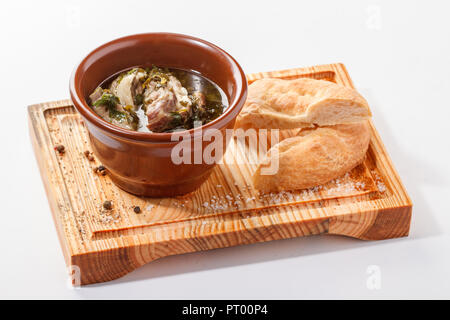 Chakapuli - traditionelle georgische Lamm Gericht mit grünen Pflaumen und Kräutern. Serviert in einem Tontopf mit Brotscheiben auf einem Holzbrett. Stockfoto