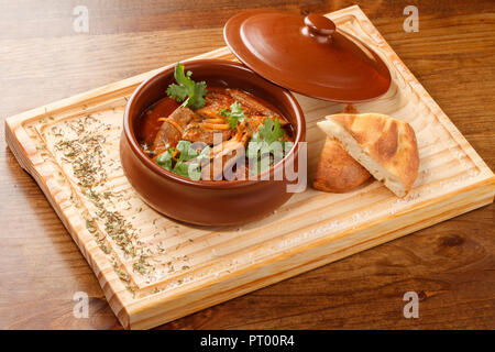 Tjvjik - Lammleber, Herz und Lunge mit Zwiebel und Tomate geschmort -. Traditionelle armenische Küche auf Holzbrett auf einem Tontopf serviert. Stockfoto