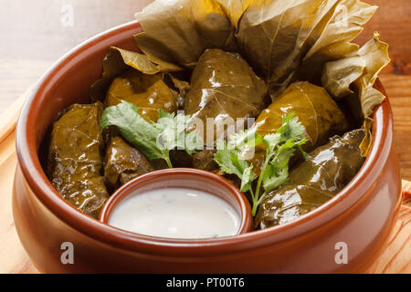 Nahaufnahme des traditionellen Dolma gefüllte Fleisch in der Weinstock treibt im Tontopf serviert mit Joghurt Sauce auf einem Holzbrett Stockfoto