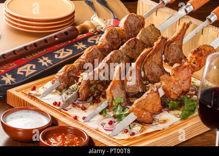 Khorovats - traditionelle armenische Kebab/Spieße Platte auf Holzbrett. Kalbfleisch, Lamm, Schweinefleisch und Hühnerspieße auf Fladenbrot serviert. Stockfoto