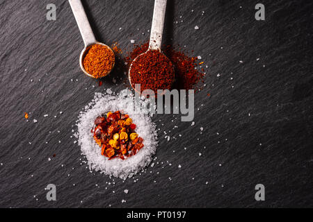 Messlöffel von Gewürzen, die bei der Herstellung von Chili auf einer Schiefertafel Hintergrund verwendet. Stockfoto