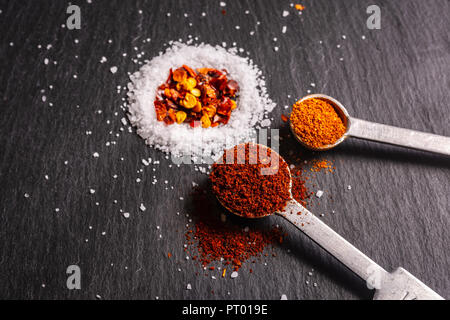 Messlöffel von Gewürzen, die bei der Herstellung von Chili auf einer Schiefertafel Hintergrund verwendet. Stockfoto