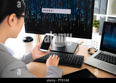 Personal im Cyber Security Unternehmen holding Handy und lesen die beschwerdeführende Nachricht vom Kunden und von der Eingabe über die Tastatur des Computers eingeben Stockfoto