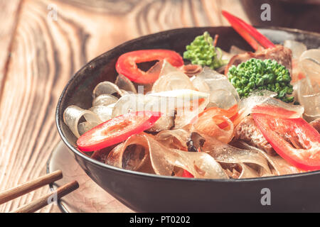 Heißen asiatischen würzigen Gericht Dicke schneiden Glasnudeln mung fungosa Bohnen süß saurer Soße Fleisch Gemüse Paprika Brokkoli in Schüssel Stäbchen am Küchentisch Sojasoße Porree. Stockfoto