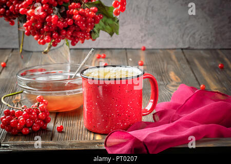 Noch immer leben Beeren eines Viburnum in ein Glas und Becher mit heißem Tee und Honig auf einer hölzernen Tisch. Herbst Konzept Ernährung, Landwirtschaft, Ernte, wärmende Getränke, Kochen Stockfoto