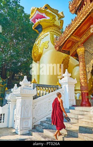 YANGON, MYANMAR - Februar 27, 2018: Der junge bhikkhu Mönch geht auf die überdachte Galerie Shwedagon Pagode mit gigantischen Statue des mythischen leogryph auf Th Stockfoto