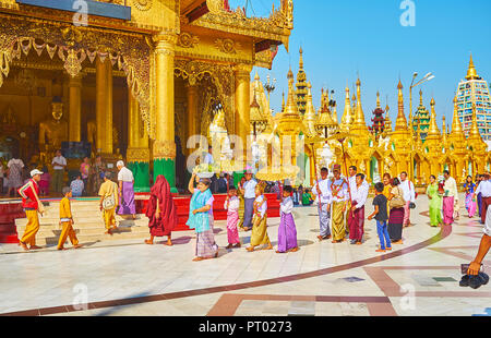 YANGON, MYANMAR - Februar 27, 2018: Buddhistische Anhänger mit goldenen Sonnenschirme am novitiation Zeremonie der Shinbyu (pabbajja), Kennzeichnung samanera monastischen Stockfoto