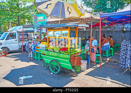 YANGON, MYANMAR - Februar 27, 2018: Die hölzerne Street Food Warenkorb mit Obst im kleinen Cafe, voll von Menschen, die in Gyar Tawya Markt, am 27. Februar i Stockfoto