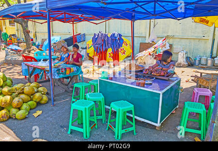 YANGON, MYANMAR - Februar 27, 2018: Der Verkäufer in Gyar Tawya Straße Markt bietet scharfe Nudeln und Grill von Schweinefleisch auf Stöcke, am 27. Februar in Yan Stockfoto