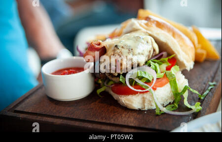 Lecker, heiß, hausgemachte tiefe Fleisch Burger auf einem frischen Salat mit geschmolzenem Käse Beschichtung der Speck und Burger mit Kartoffelecken und Roll serviert. Stockfoto