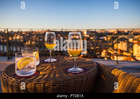 Zwei Gläser white Porto und zwei Gläser mit funkelndem Wasser auf der Terrasse bei Sonnenuntergang, mit der Stadt Porto, die in der fernen Hintergrund Stockfoto