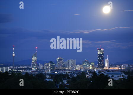 Vollmond und Wolken über der Skyline der Wiener SPÖ. Die moderne Stadt mit Wolkenkratzern mit beleuchteten Fenstern an düsteren Abend. Stockfoto