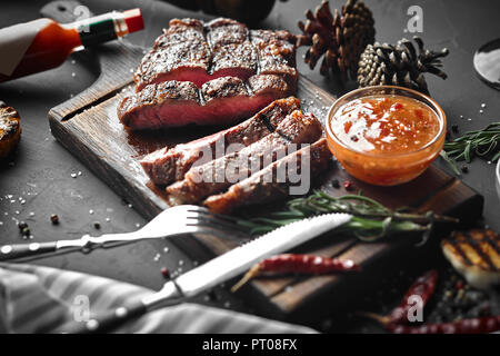 Gegrilltes Steak in Stücke geschnitten, mit Gewürzen und Öl auf schwarzem Hintergrund eingerichtet. Ansicht von oben. Kopieren Sie Platz. Immer noch leben. Flach Stockfoto