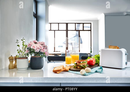 Weiß elektrische Toaster mit Orangensaft mit Sandwich am Küchentisch. Frühstück in der gemütlichen Küche. Nützliches und leckeres Essen Stockfoto