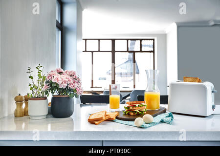 Weiß elektrische Toaster mit Orangensaft mit Sandwich am Küchentisch. Frühstück in der gemütlichen Küche. Nützliches und leckeres Essen Stockfoto