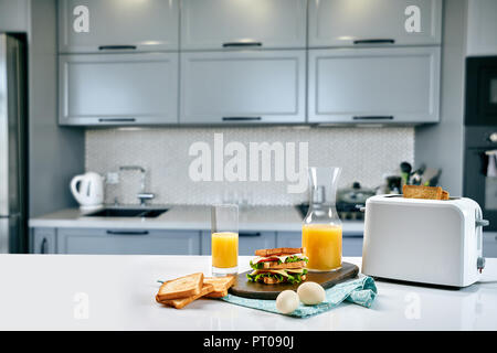 Weiß elektrische Toaster mit Orangensaft mit Sandwich am Küchentisch. Frühstück in der gemütlichen Küche. Nützliches und leckeres Essen Stockfoto