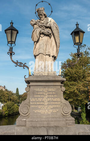 Kortrijk, Flandern, Belgien - 17. September 2018: grau beige Statue des Hl. Johannes von Nepomuk auf der Brücke Broeltürmen unter blauem Himmel. Einige grüne Foli Stockfoto