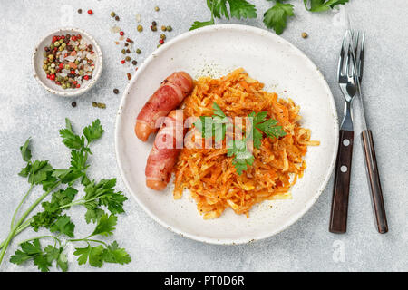 Gedünstetem Rosenkohl mit Karotten, Zwiebeln und Tomaten und Würstchen im Speckmantel mit Petersilie und Gewürzen in eine weiße Platte. Bigos. Ein leckeres Mittagessen. Selektive foc Stockfoto