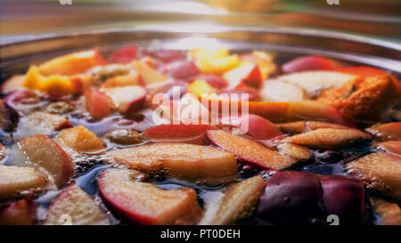 Bunte Apfelscheiben, Obst Mix in einem Topf. Erfrischende Frucht Apfelwein Punsch Party Trinken. Organische Nahrung Warm Glow Hintergrund. Stockfoto