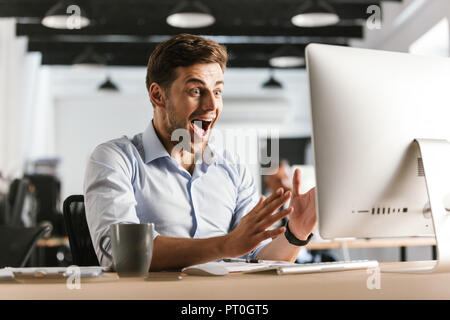 Entsetzt schreien Geschäftsmann mit Computer während der Sitzung durch die Tabelle im Büro Stockfoto