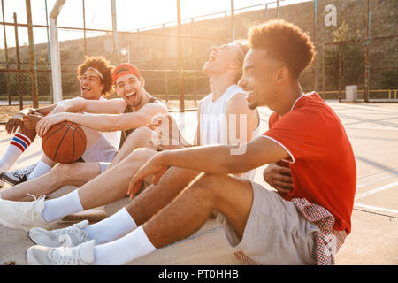 Gruppe von Lachen multiethnischen Freunden Basketball Spieler auf dem Sportplatz Sitzen, Reden Stockfoto