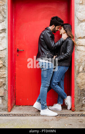 Liebevolle junge Paar Küssen an der roten Tür Stockfoto