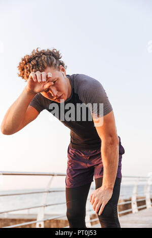 Porträt einer verschwitzten Sportler Ausruhen nach Workout am Strand, Musik hören mit Kopfhörern Stockfoto