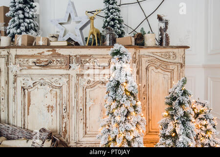 Geschmückter Weihnachtsbaum auf hölzerne Kommode Kommode Kommode in weiße Interieur mit künstlichen Blumen, Girlanden und Spielzeug Stockfoto