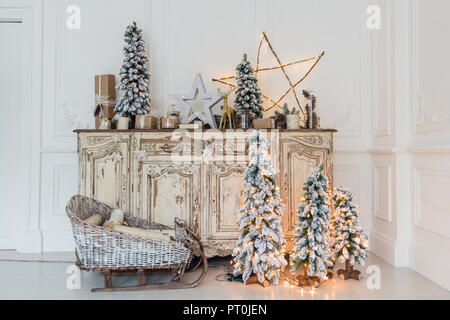 Geschmückter Weihnachtsbaum auf hölzerne Kommode Kommode Kommode in weiße Interieur mit künstlichen Blumen, Girlanden und Spielzeug Stockfoto