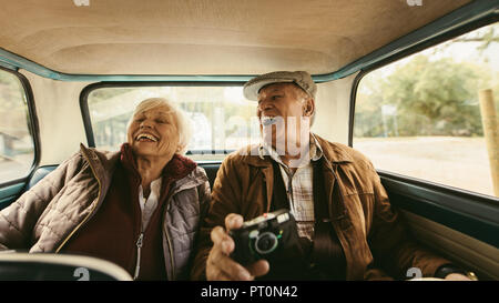 Freundliche alte Paar saß auf dem Rücksitz Ihres Autos und Lachen. Älterer Mann und Frau genießen, die zusammen reisen von einem alten Auto. Stockfoto