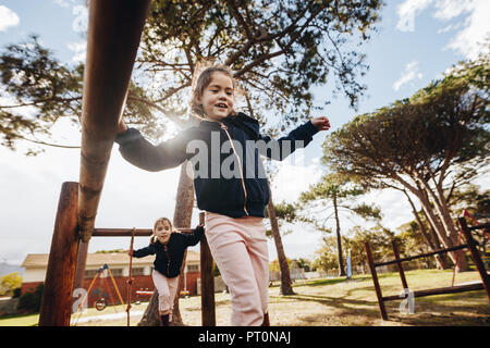 Süße kleine Mädchen mit ihrer Zwillingsschwester Spielen am Spielplatz im Freien an einem sonnigen Tag. Zwei Mädchen, die an der öffentlichen Park. Stockfoto