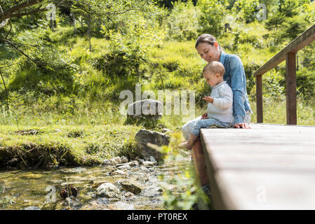 Mutter und Tochter sitzen auf Holzbrücke, Mountain Stream Stockfoto