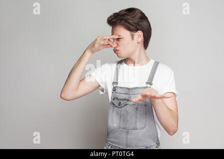 Schlechter Geruch, von hier fortgehen. Junge brunette Mann im lässigen Stil mit weißen T-Shirt und Jeans Overalls stehen, kneifen Nase und Ablehnung oder bannin Stockfoto