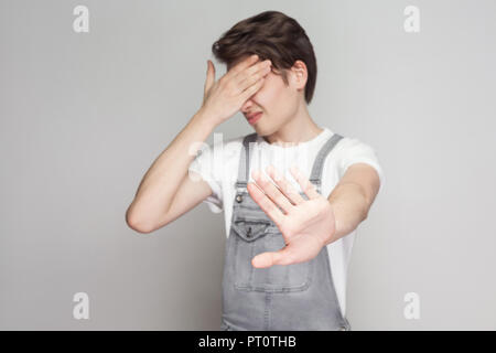 Portrait von Angst oder Scheu junge brunette Mann im lässigen Stil mit Jeans Overalls ständigen geschlossenen Augen mit den Händen, Sperrung und verbot Geste. Stockfoto