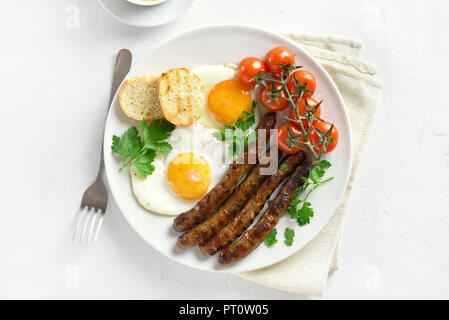 Teller zum Frühstück. Gebratene Eier, Würstchen und Kirschtomaten auf die Platte über der weißen Stein Hintergrund. Ansicht von oben, flach Stockfoto
